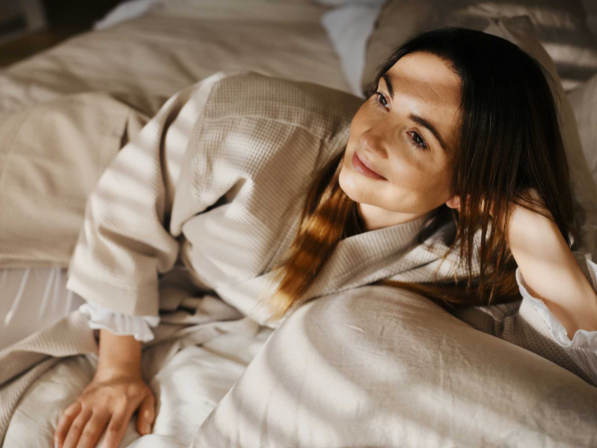 Woman laying on her side in bed with her head perched on her hand looking out at the morning light