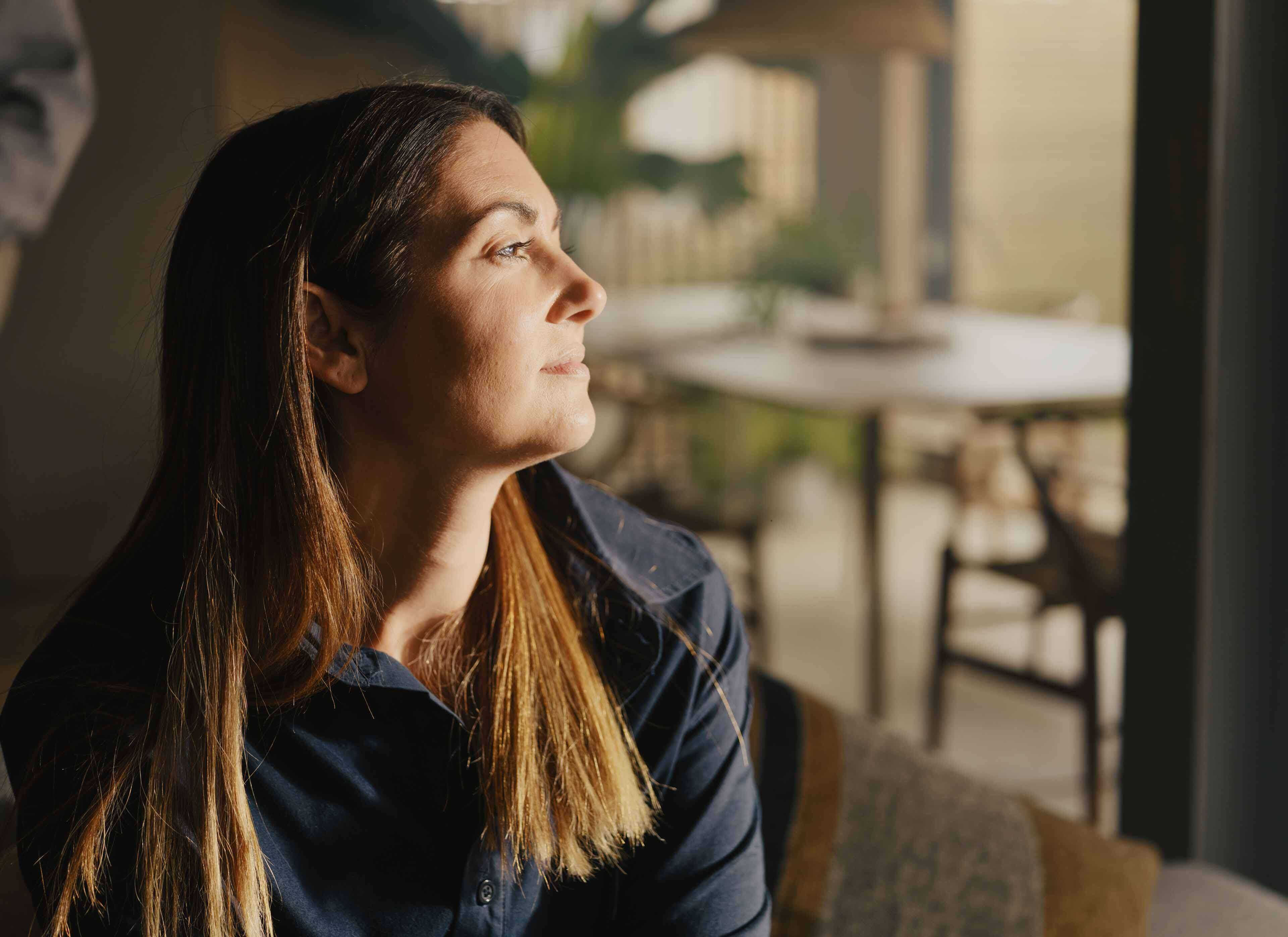 Woman looking out with morning sunlight hitting her face with an unrested look on her face